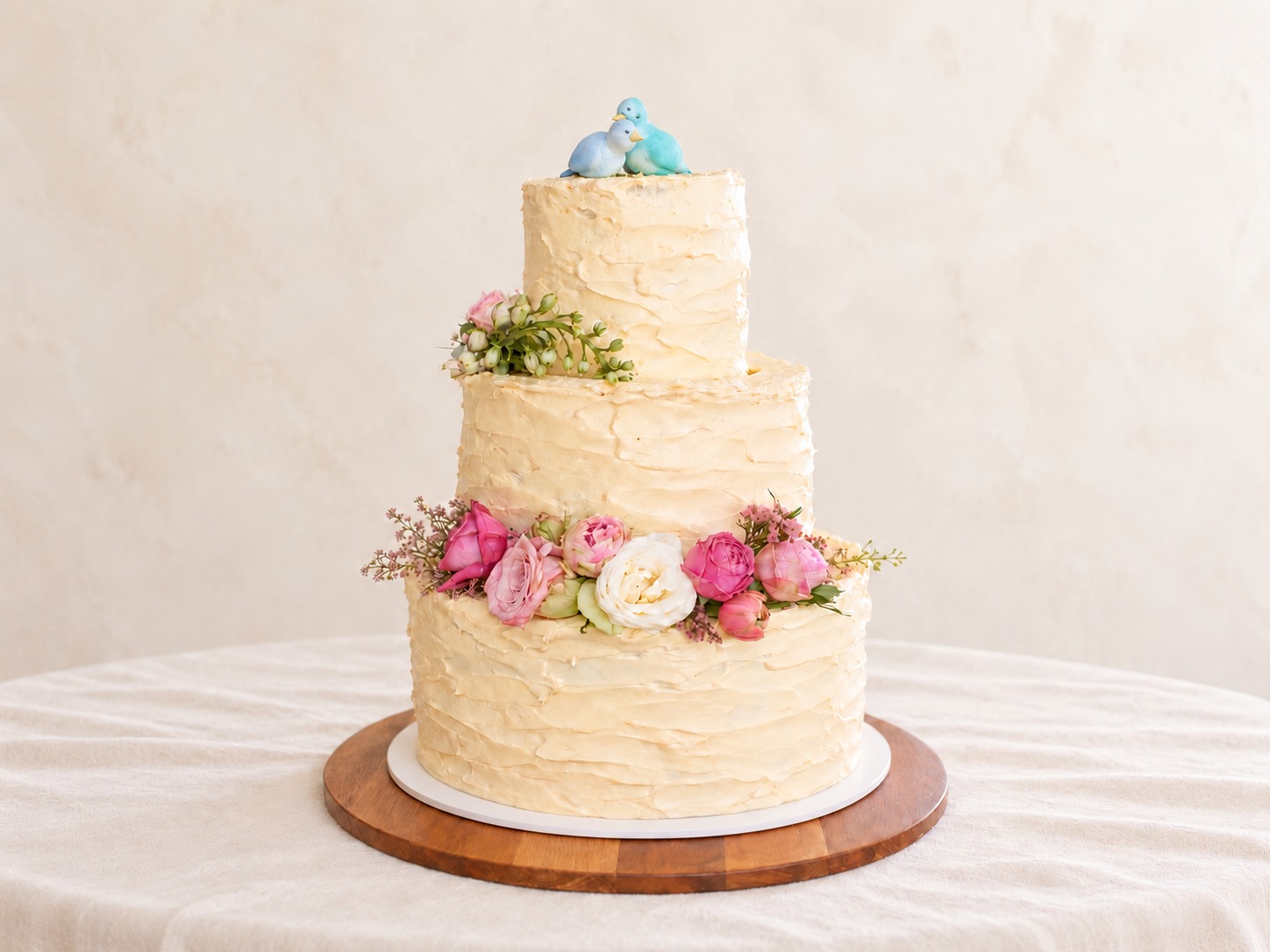 Rustic three-tier ivory wedding cake with pink flowers and two lovebirds